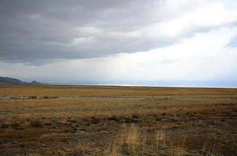 Flat dried steppe at the foot of the mountains under a cloudy autumn sky. Stock Photos
