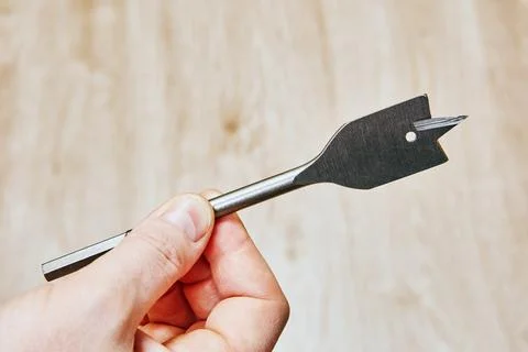 Flat drill bit with sharp cutting edges and small round hole near tip held .. Stock Photos