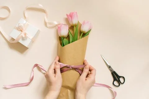 Flat female hands tie a satin ribbon bow on a simple bouquet of fresh pink tu Stock Photos