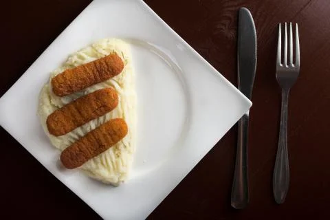 Flat lay above fish sticks served with mashed potatoes with silverware Stock Photos