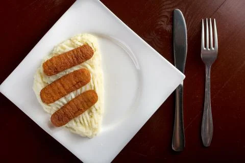 Flat lay above fish sticks served with mashed potatoes with silverware Stock Photos