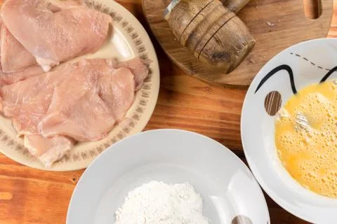 Flat lay above wooden table with raw chicken breasts mixed eggs flour and woo Foto stock