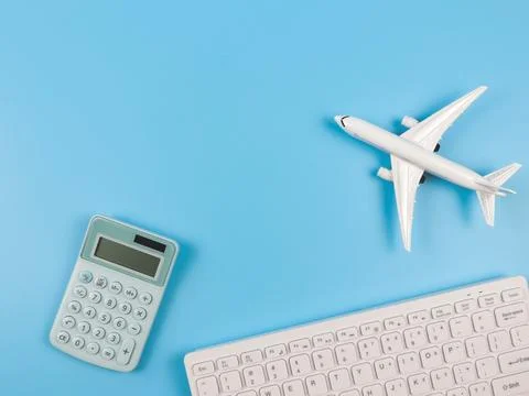 Flat lay of airplane model, computer keyboard, and blue calculator on blue .. Stock Photos