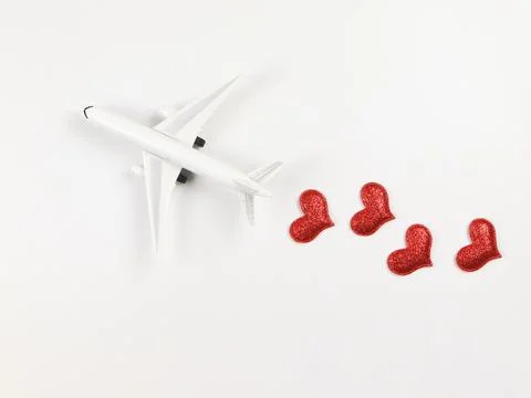 Flat lay of airplane model with red hearts on white background. Honeymoon t.. Stock Photos