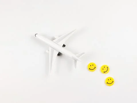 Flat lay of airplane model with three yellow circle smiling faces  on white.. Stock Photos