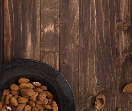 Flat lay of almonds in black plate with other accessories on brown wooden bac Stock Photos