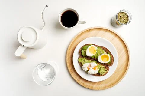 Flat lay avocado toast with eggs on dark bread, black coffee and glass of water Stock Photos