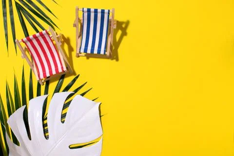 Flat lay of beach deck chairs, monstera and palm leaves on yellow background Stock Photos