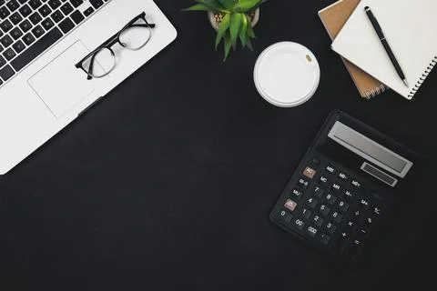 Flat lay black background with laptop, coffee cup and calculator, top view. Stock Photos