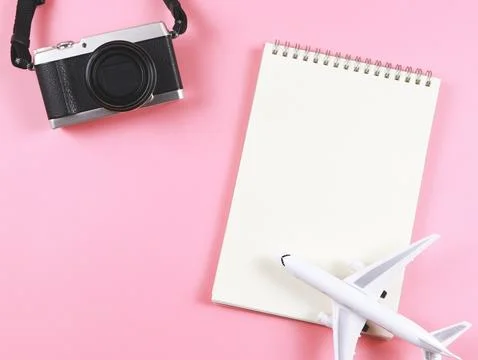 Flat lay of blank page opened notebook, airplane model  and camera on pink .. Stock Photos