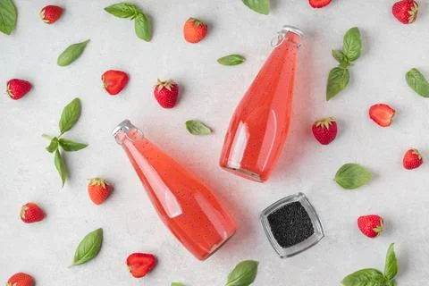 Flat lay with bottles of delicious basil seeds strawberry drink on grey table Stock Photos