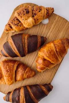 Flat lay of bunch of appetizing brown and chocolate croissants on a wooden board Stock Photos