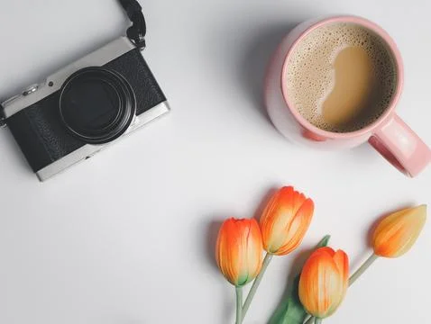 Flat lay of camera, pink cup of coffee, and red yellow tuips on white backgro Stock Photos