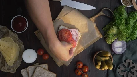 Flat lay of chef's hand adds sliced tomato to the sandwich with ham and Stock Footage 113186474