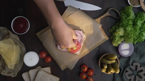 Flat lay of chefs hand adds sliced tomatoes to the sandwich Video stock 143783524