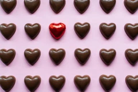 Flat lay with chocolate hearts featuring one candy in a red foil standing out Stock Photos