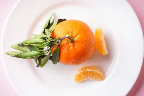 Flat lay close-up mandarin with a green branch and slices in a white plate on Stock-Fotos
