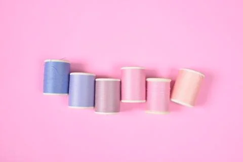 Flat lay of colored thread rolls for sewing on pink background, Sewing and ne Stock Photos