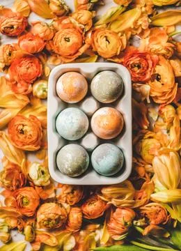 Flat-lay of colorful dyed Easter eggs over blooming orange flowers Stock Photos