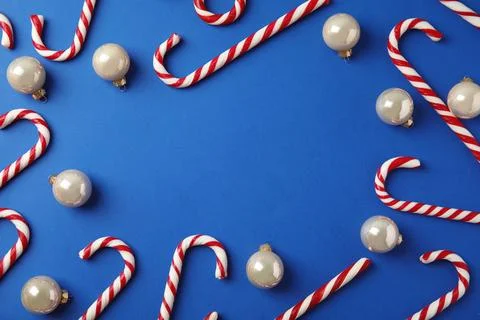 Flat lay composition with candy canes and Christmas balls on blue background. Stock Photos
