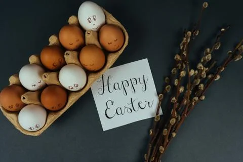 Flat lay composition of Easter eggs with painted faces in carton box and willow Stock Photos