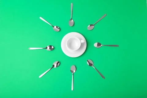 Flat lay composition of empty cup and new teaspoons on green background Stock Photos