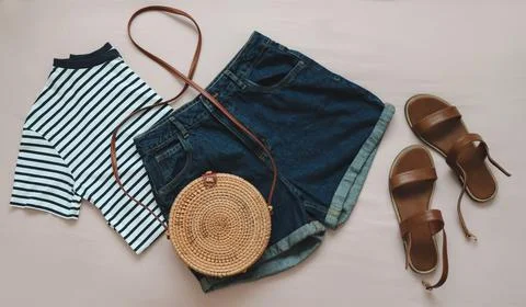 Flat lay composition with female top, denim shorts, sandals and a wicker rattan Stock Photos