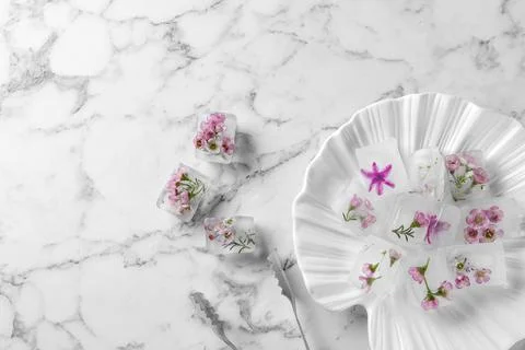 Flat lay composition with floral ice cubes on marble background. Space for te Stock Photos