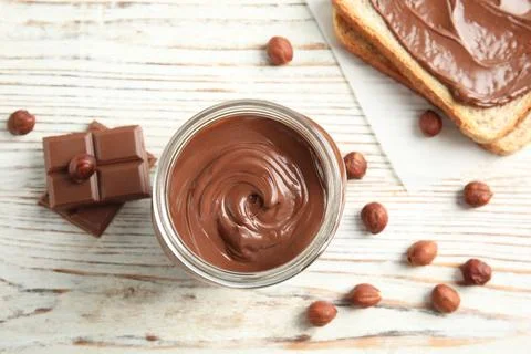 Flat lay composition with glass jar of tasty chocolate cream, bread and hazel Stock Photos