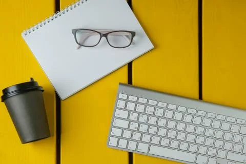 Flat lay composition with glasses, coffee, notepad and keyboard on a yellow w Stock Photos