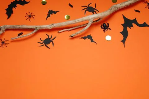 Flat lay composition with paper bats, spiders and wooden branch on orange bac Stock Photos