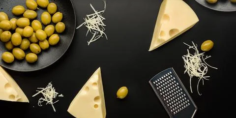 Flat lay composition with pieces of cheese and olives on a dark background. Stock Photos