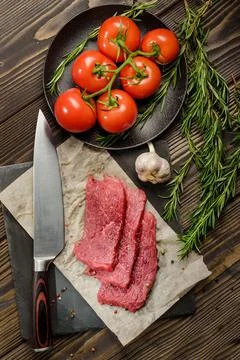 Flat lay composition with pieces of raw beef, kitchen knife, tomatoes and ros Stock Photos