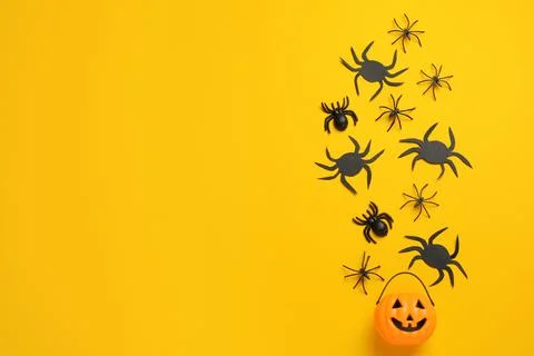 Flat lay composition with plastic pumpkin basket and spiders on yellow backgr Stock Photos