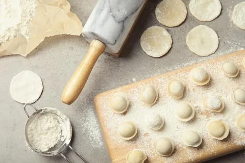 Flat lay composition with raw dumplings on grey background. Process of cookin Stock Photos