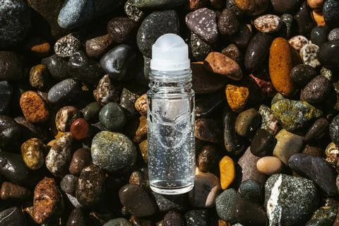 Flat lay composition of a roll on transparent deodorant bottle on wet beach Foto stock