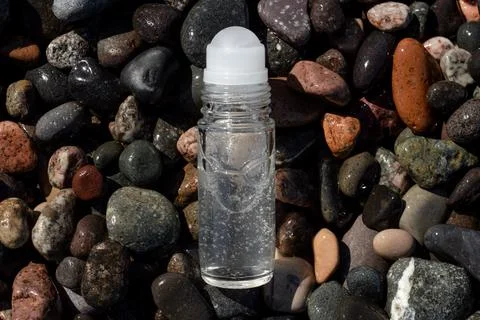 Flat lay composition of a roll on transparent deodorant bottle on wet beach Stock Photos