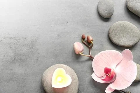 Flat lay composition with spa stones, orchid pink flower and heart on grey. Stock Photos