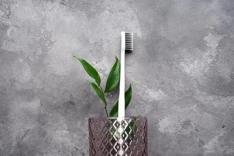 Flat lay composition of a white toothbrush in a glass on a gray background. S Foto stock
