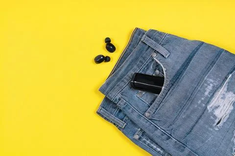 Flat lay composition with wireless earbuds, jeans and charging case in its po Stock Photos