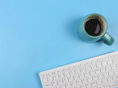 Flat lay of computer keyboard, blue cup of black coffee on blue  background w Foto stock