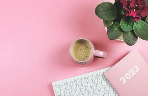 Flat lay of computer keyboard, pink coffee cup  pink diary 2023 and African.. Stock Photos