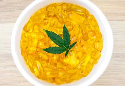 Flat lay of container filled with CBD soft gel capsules and Cannabis leaf Stock Photos