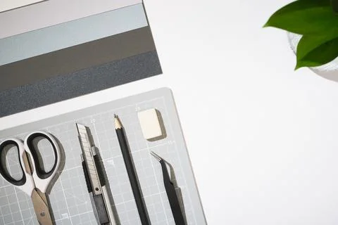 Flat lay of craft tools and stationery on a white desk. Grey cutting mat, sci Stock Photos