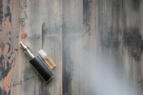 Flat lay of e-cigarette and e-liquid on wooden background, covered smoke Stock Photos