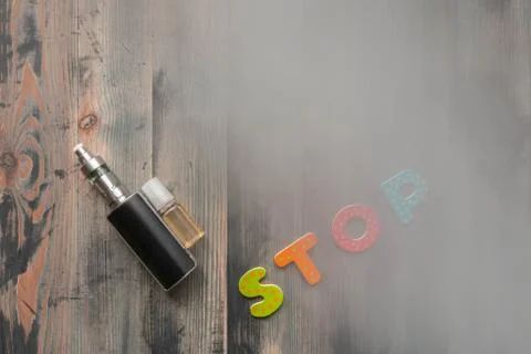 Flat lay of e-cigarette, e-liquid, and letters stop on wooden background, cov Stock Photos