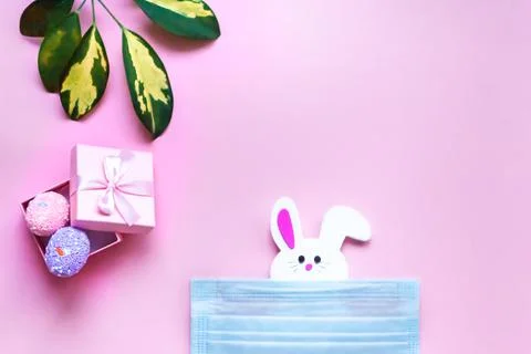 Flat lay easter pink background with bunny in medical mask and painted eggs Stock Photos