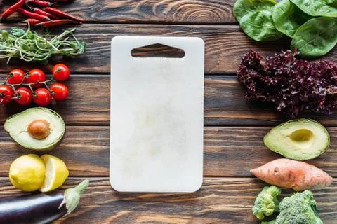 Flat lay with empty cutting board and fresh vegetables arranged around on woo Stock-Fotos