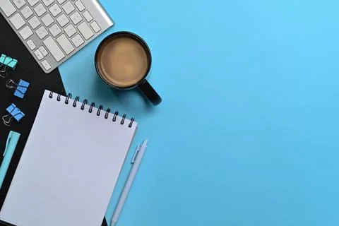 Flat lay empty notebook, coffee cup and keyboard on blue background. Stock Photos