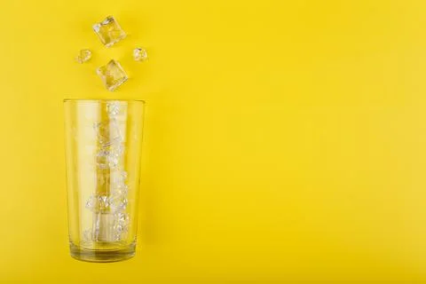 Flat lay with empty transparent glass with spilled ice cubes on yellow Stock Photos